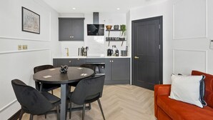 A compact kitchen with modern appliances, a dining area with a round table and chairs, and a cozy red sofa.