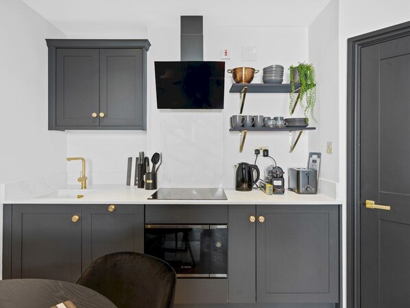 Una cocina compacta con armarios oscuros, encimera blanca, horno Bosch y televisor montado.