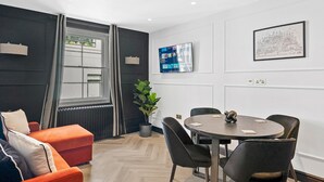 A modern room with a round table, black chairs, a red sofa, and a large window with curtains.