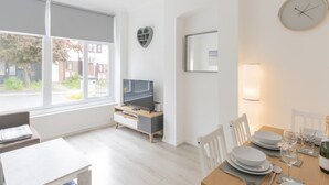 En moderne stue med fjernsyn, spisebord til to og et stort vindue med udsigt ud.