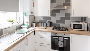 Et moderne køkken med hvide skabe, en gasblus, en mikrobølgeovn og en vask.