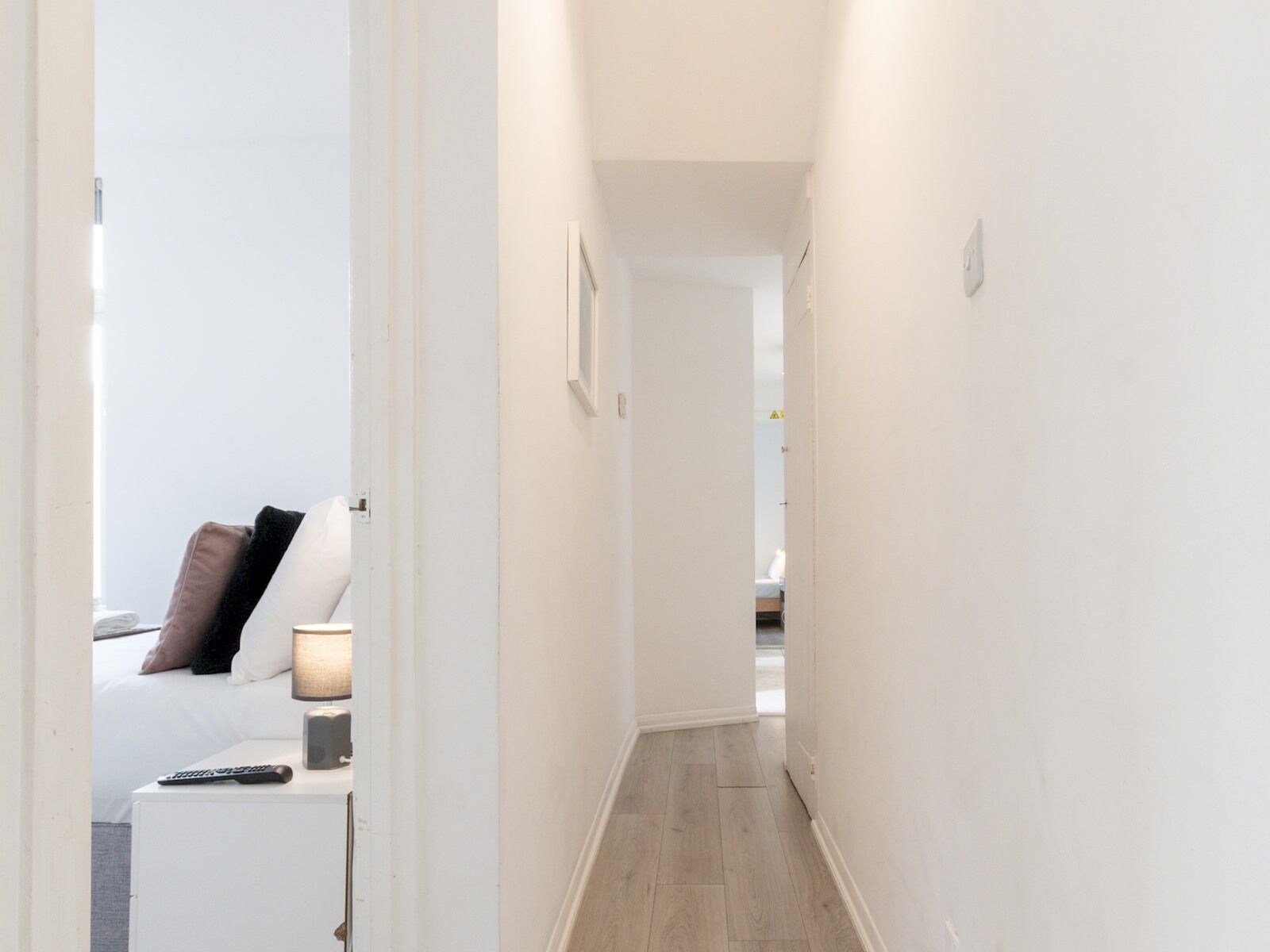 Un couloir étroit, avec un lit et une table de chevet au fond.