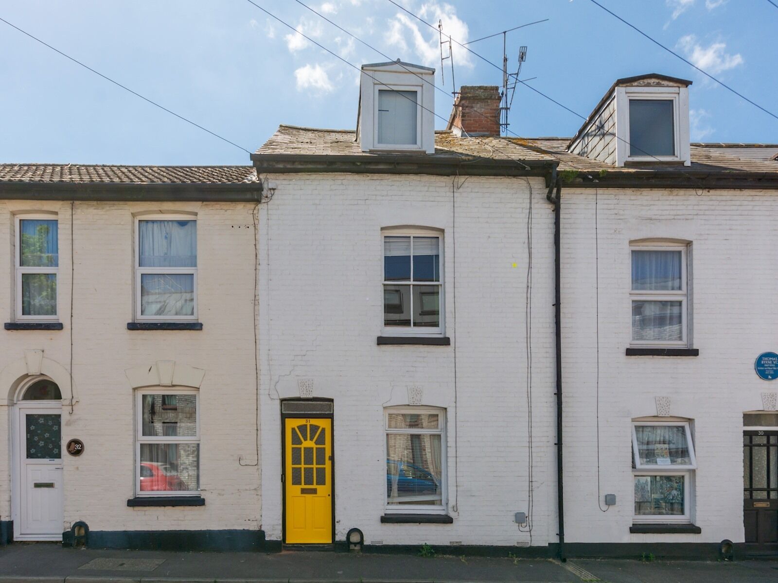 A row of white brick townhouses with a yellow door, numbered windows, and a blue sign on the right.