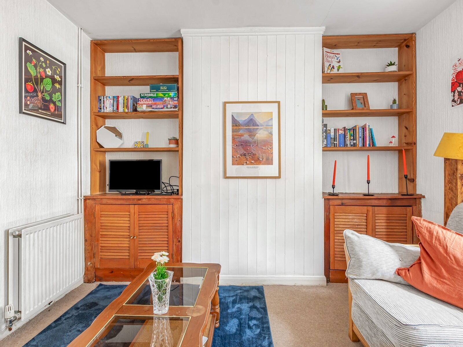 A cozy living room with a television, wooden shelves, and a framed picture on the wall.