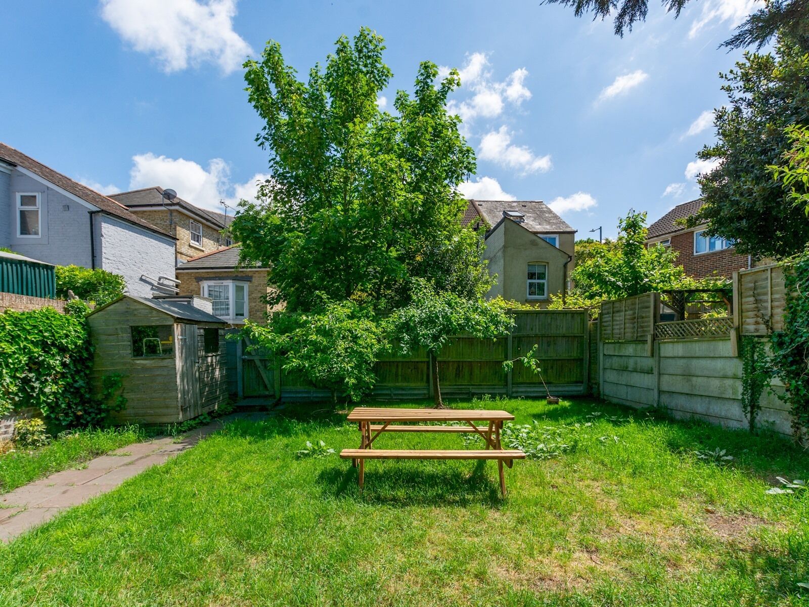 A backyard with a wooden picnic table, a small shed, and a tall tree.