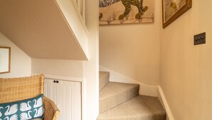 Una escalera con alfombra color crema, una silla de mimbre con un cojín con forma de cisne y un mural de tigre en la pared.