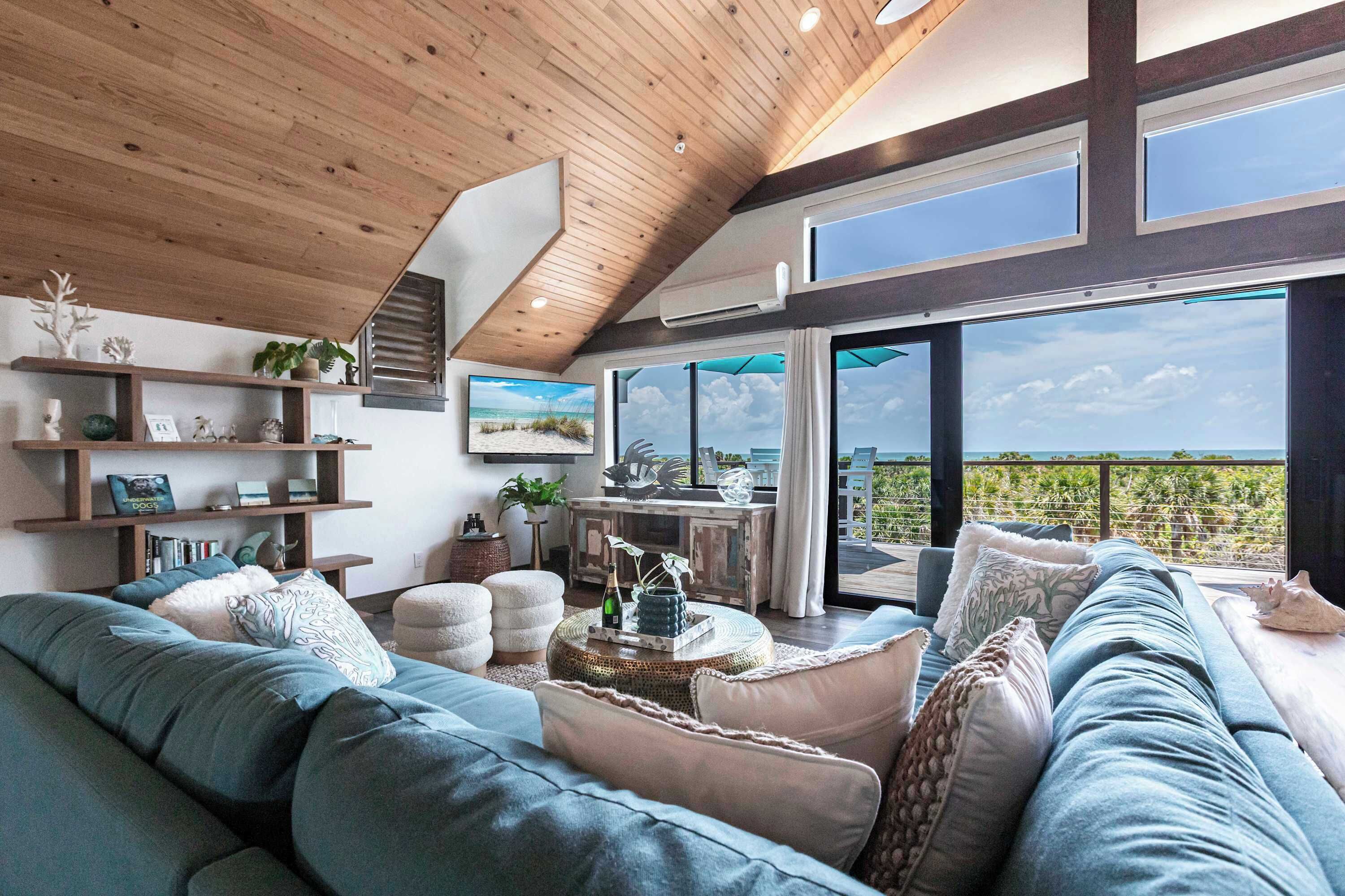 A modern living room with a large sectional sofa, a coffee table, and a view of the outdoors through large windows.