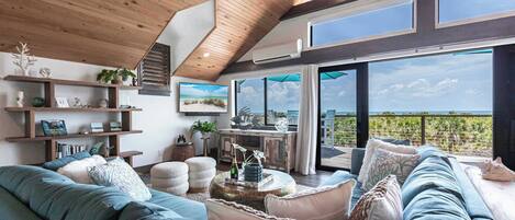 A modern living room with a large sectional sofa, a coffee table, and a view of the outdoors through large windows.