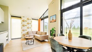 A modern living room with a sectional sofa, a dining table with chairs, and a large window offering a view of the outdoors. - Tranquil Holiday Home With Views (Oud Ade)