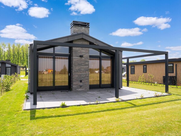 A modern outdoor patio with a stone fireplace, large sliding glass doors, and a metal pergola structure. - Tranquil Holiday Home With Views (Oud Ade)