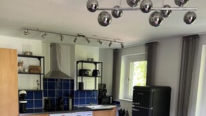 Une cuisine moderne équipée d’un four encastré, d’une machine à café et d’un réfrigérateur noir. Le salon comprend un canapé bleu et une table à manger.