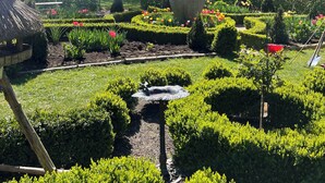 Un jardin avec des haies soigneusement taillées, un grand vase en pierre et, au fond, un bâtiment doté d’un toit en tuiles.
