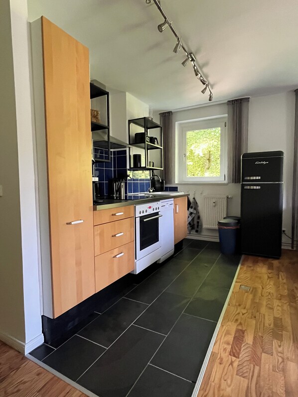 A compact kitchen with a built-in oven, a refrigerator, and a window with a view of greenery. - Apartment Castanea (Ivenack OT Markow)