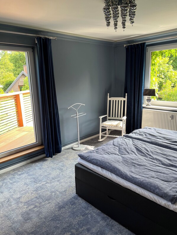 A bedroom with a bed, a chair, a radiator, and a window with curtains.