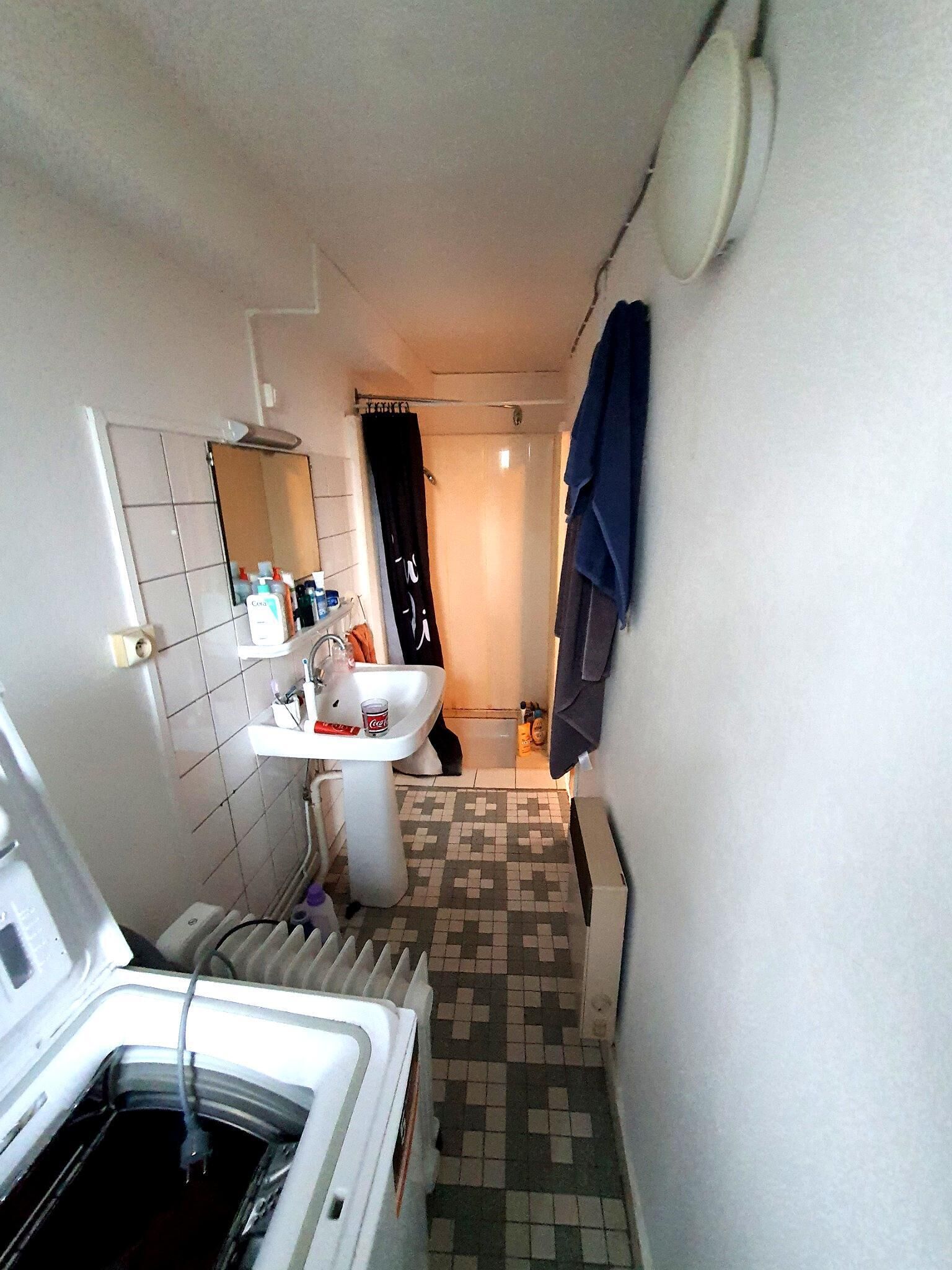 Un baño estrecho con lavamanos, espejo y suelo de baldosas.