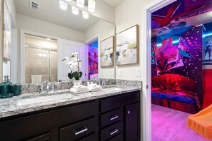A modern bathroom with a granite countertop, a large mirror, and a sink. There is a potted orchid on the counter. - Mega Themed Villa Near Disney w/ Pool & Arcade (Clermont)