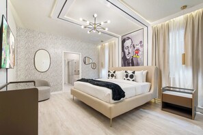 A modern bedroom with a large bed, a bedside table, a chair, and a unique ceiling light fixture. - Mega Themed Villa Near Disney w/ Pool & Arcade (Clermont)