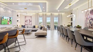 A modern kitchen with a marble backsplash, a dining area with a long table and chairs, and a living area with a sofa and a TV.