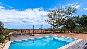 Ein rechteckiger Pool mit Holzterrasse und Liegestühlen, umgeben von einem Zaun und Bäumen.