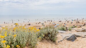 A beach with people, yellow flowers, and rocks. - Le Cocon Vendéen - Vue Mer (Saint-Hilaire-de-Riez)