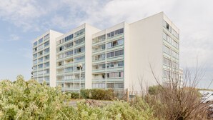 A multi-story hotel with a modern design, featuring balconies on each floor and a parking area in the foreground. - Le Cocon Vendéen - Vue Mer (Saint-Hilaire-de-Riez)