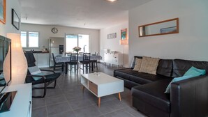 A modern living room with a black leather sofa, a white coffee table, and a dining area with a table and chairs. - La Bulle de Landrezac - Jacuzzi/Proche Plage (Sarzeau)