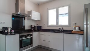 A modern kitchen with white cabinets, a stainless steel refrigerator, a microwave, a coffee maker, and a window providing natural light. - La Bulle de Landrezac - Jacuzzi/Proche Plage (Sarzeau)