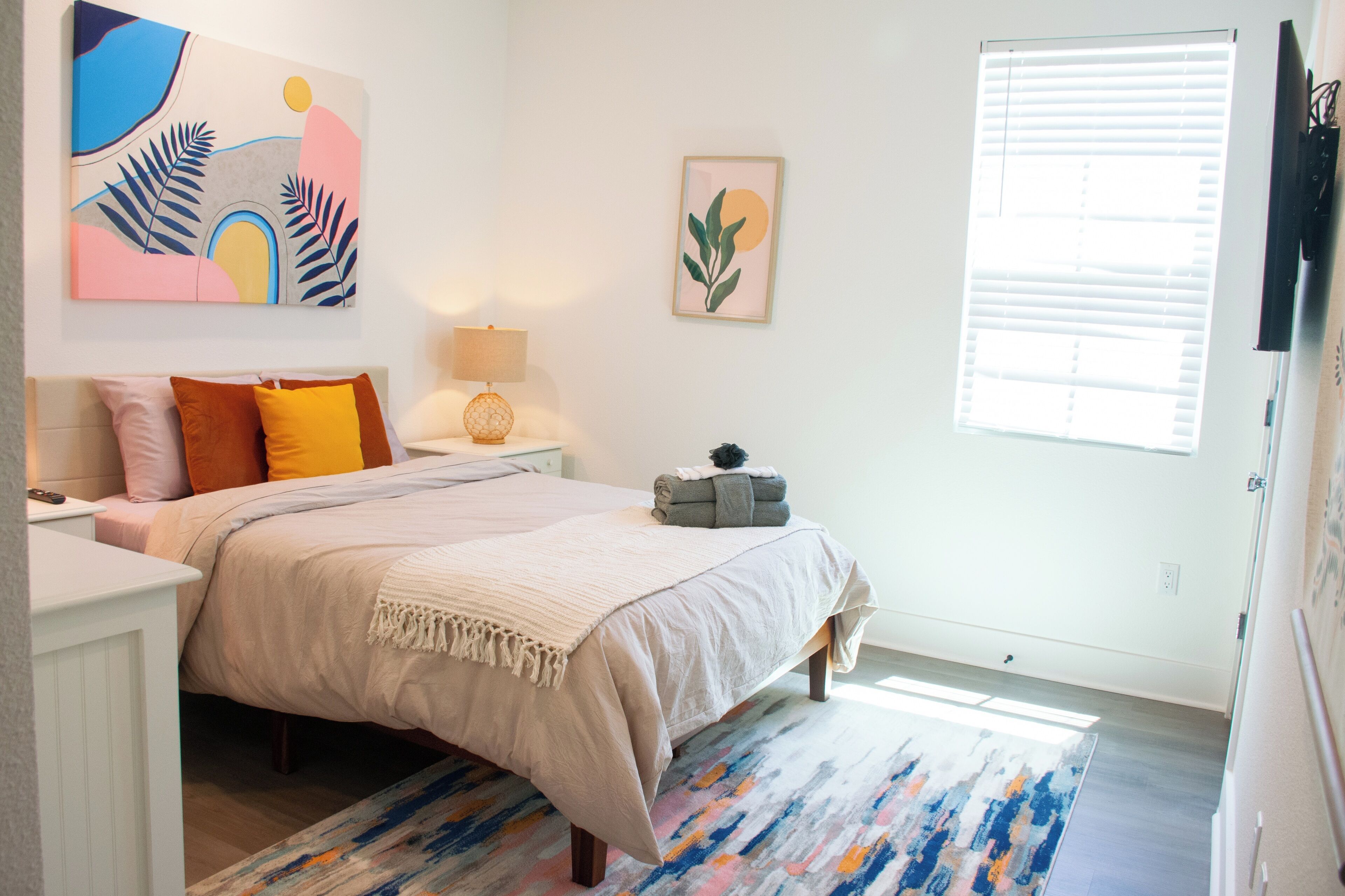 Une chambre à coucher avec un lit, une table de chevet, une lampe et des œuvres d’art accrochées aux murs.