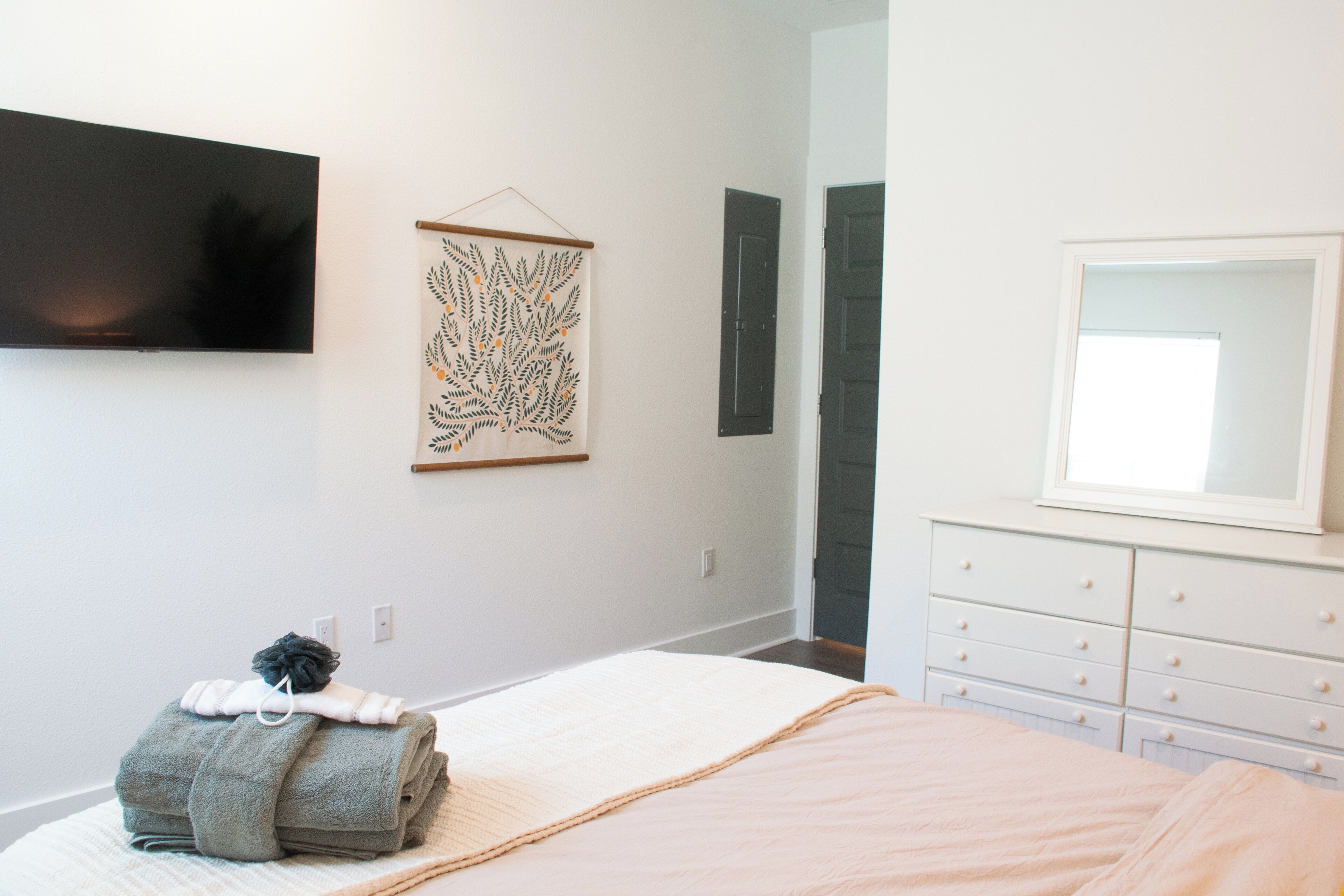 Un dormitorio con una cama, un televisor montado en la pared, un aparador y una obra de arte enmarcada en la pared.