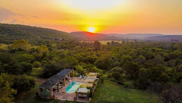 A villa with a pool, surrounded by dense forest and hills.