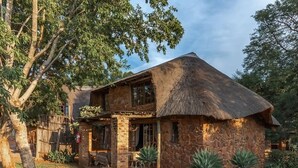 A stone house with a thatched roof, a wooden porch, and a small garden with agave plants.