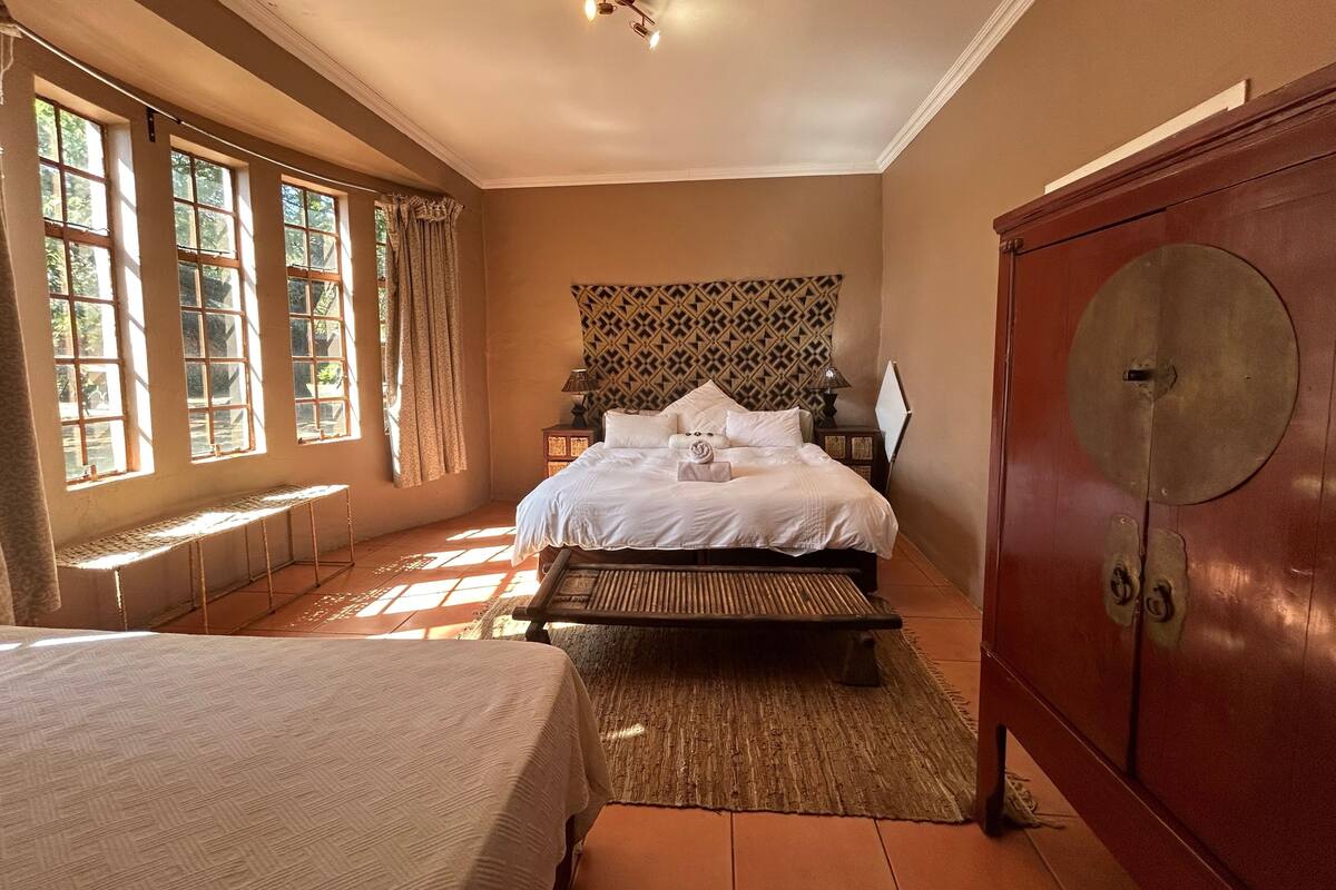 A bedroom with a bed, a bench, a wardrobe, and a patterned headboard.