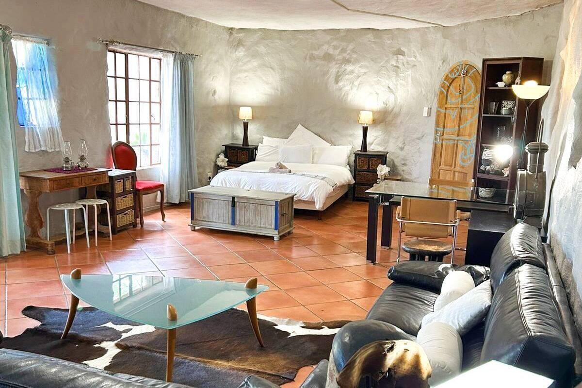 A spacious room with a bed, a glass table, a leather sofa, a desk, and a chair.