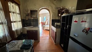A rustic kitchen with a tiled floor, wooden cabinets, a refrigerator, and a window with curtains.