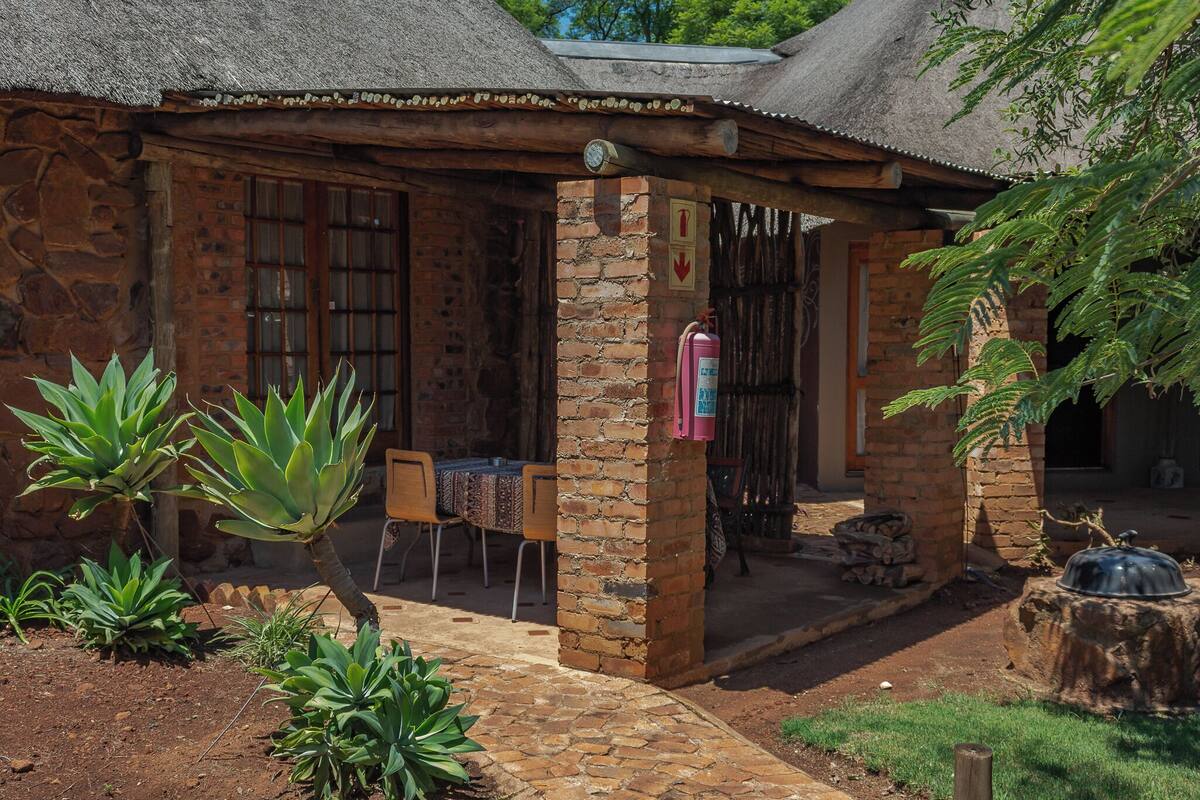 A rustic stone building with a thatched roof, a small outdoor seating area, and a fire extinguisher mounted on the wall.