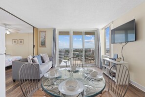 A modern living room with a glass dining table, grey sofa, and a balcony with a city view.