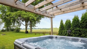 A hot tub under a wooden pergola with a grassy yard and trees in the background.