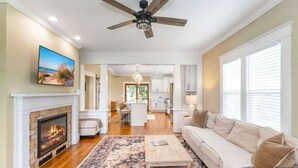 A spacious living room with a fireplace, a ceiling fan, and a view into the kitchen.
