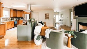 A modern kitchen with wooden cabinets, a central island, and a built-in stove. There is a seating area with a sofa and a coffee table.