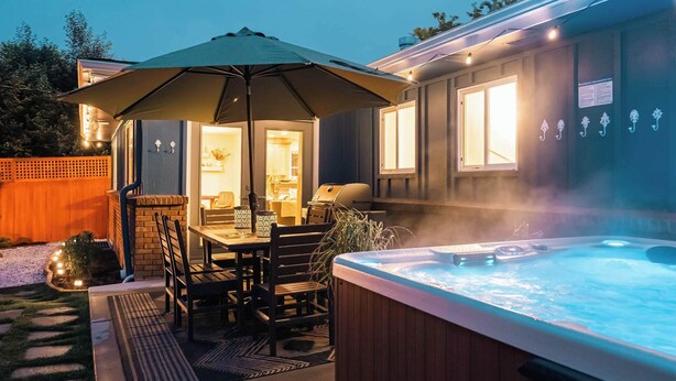 A hot tub with a wooden deck and a table with chairs under an umbrella.