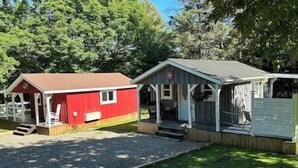 A red cabin with a porch and a blue cabin with a covered porch. - Cozy Coastal Cabin w/Hot Tub (Valley Road)