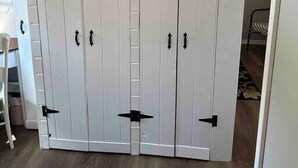 A large white wardrobe with black handles and corner brackets, located in a room with wooden flooring and a sloped ceiling. - Cozy Coastal Cabin w/Hot Tub (Valley Road)