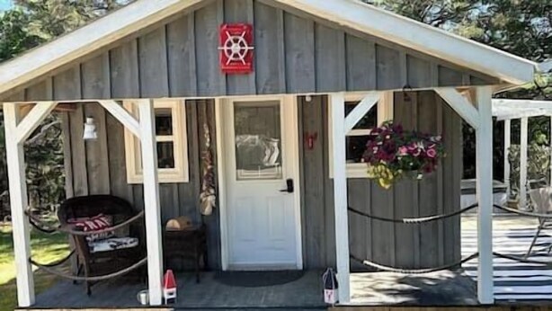 A wooden cabin with a porch, a door, and a small window. - Cozy Coastal Cabin w/Hot Tub (Valley Road)