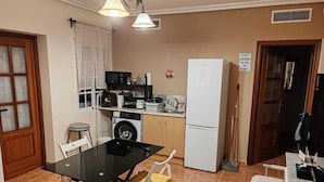 A compact kitchen with a washing machine, a refrigerator, a dining table with chairs, and a sign indicating quiet hours. - Come and stay in Marifé's house, two bedrooms available at 17 km from Seville. (Villanueva del Ariscal)