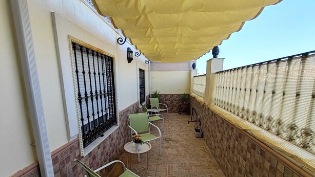 A balcony with a yellow canopy, green chairs, a small table, and a potted plant. - Come and stay in Marifé's house, two bedrooms available at 17 km from Seville. (Villanueva del Ariscal)