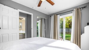 Un dormitorio con una cama grande, un ventilador de techo y un ventanal corredera que da a un balcón.