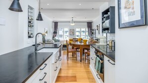 A modern kitchen with a black countertop, wooden dining table, and pendant lighting.