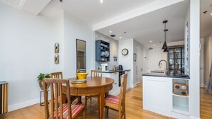 A modern kitchen with white cabinetry, a round wooden dining table, and a built-in island with a black countertop.