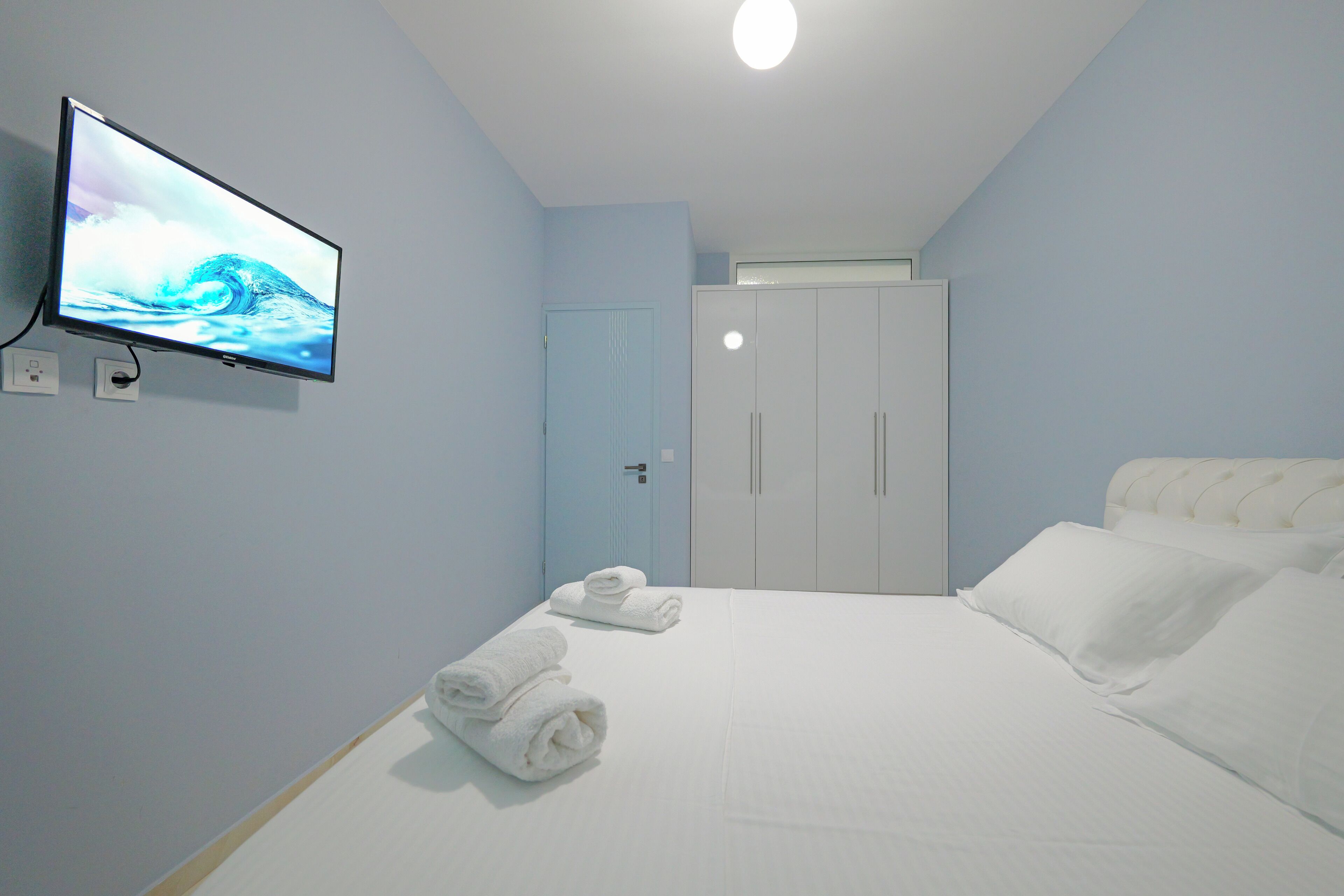 A hotel room with a bed, a TV mounted on the wall, a wardrobe, and a door.