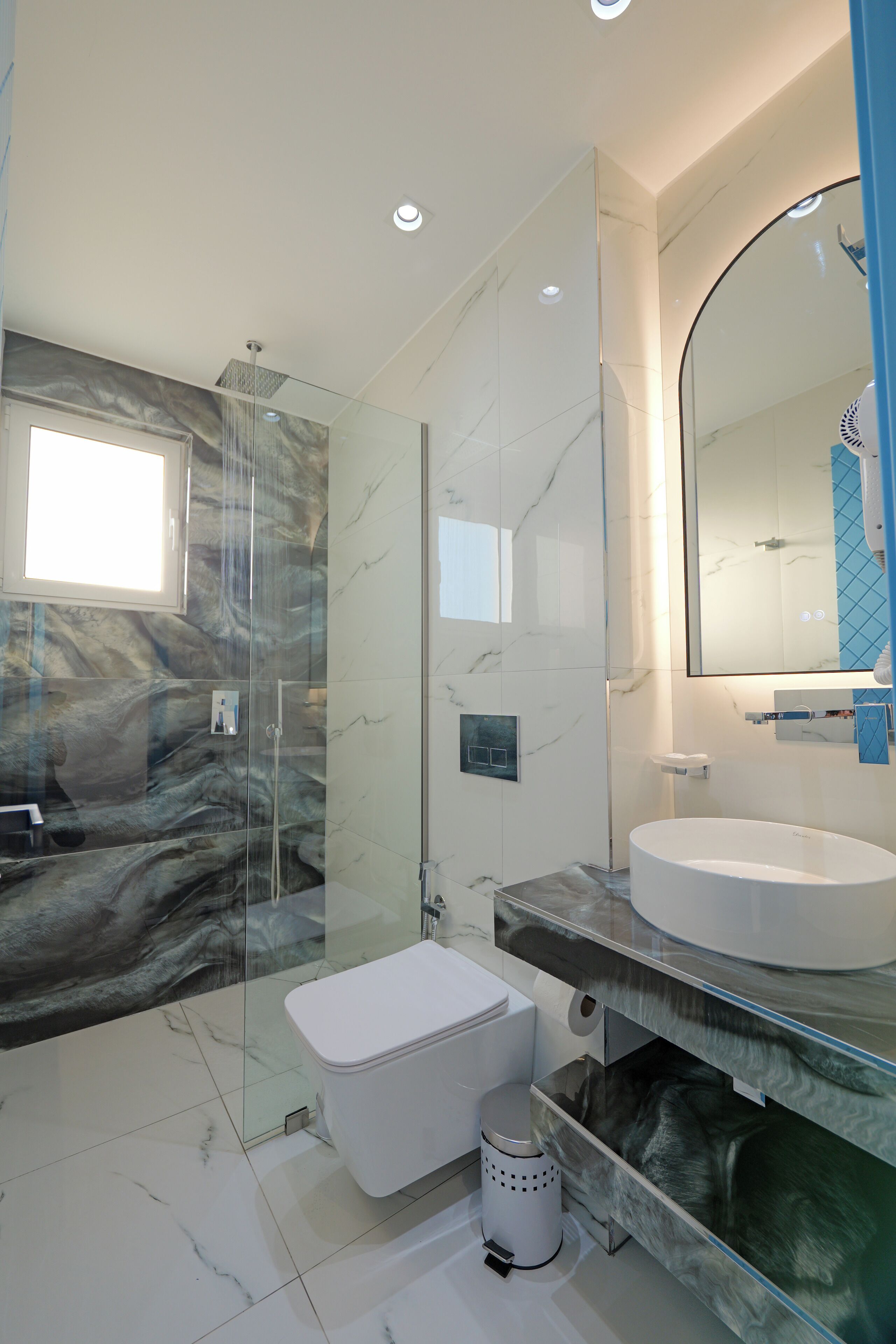 A modern bathroom with a glass-enclosed shower, a marble backsplash, and a large mirror above the sink.